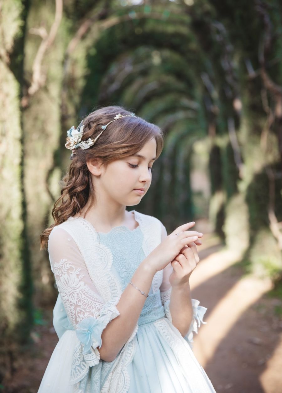 Niña de comunión con corona de flores en un túnel de árboles