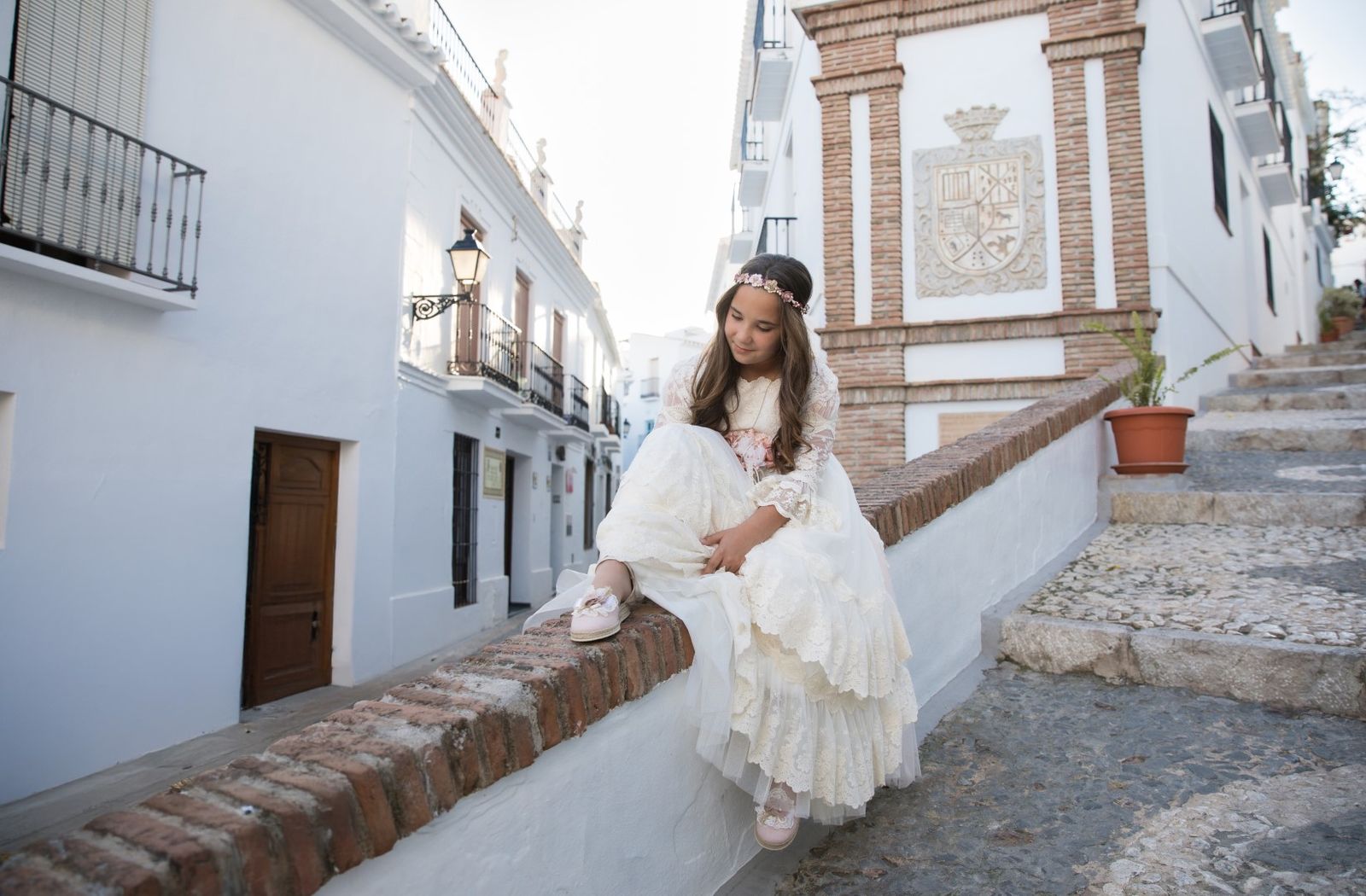 Niña de comunión sentada en una calle blanca del pueblo