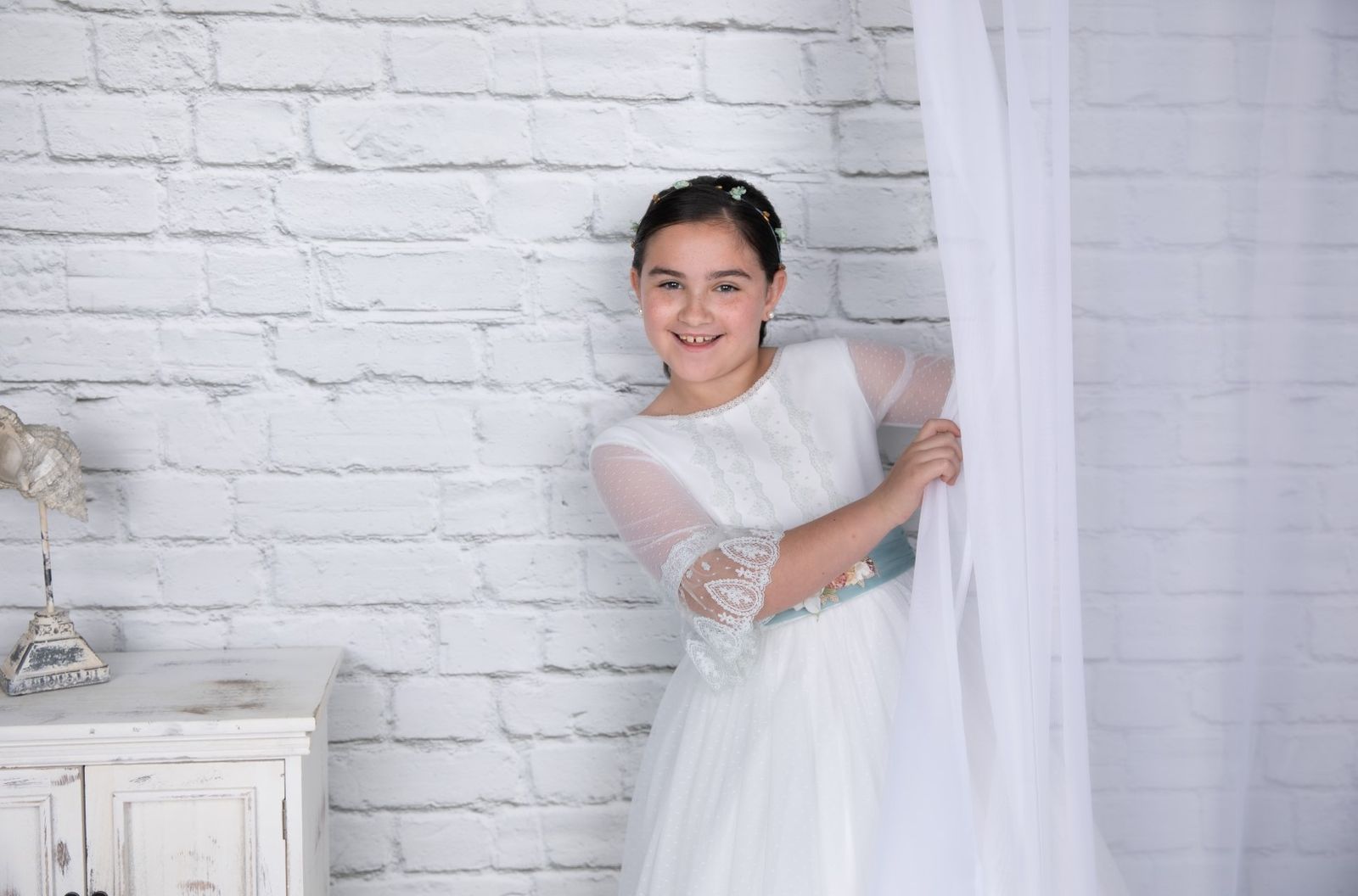 Niña de comunión junto a una cortina blanca