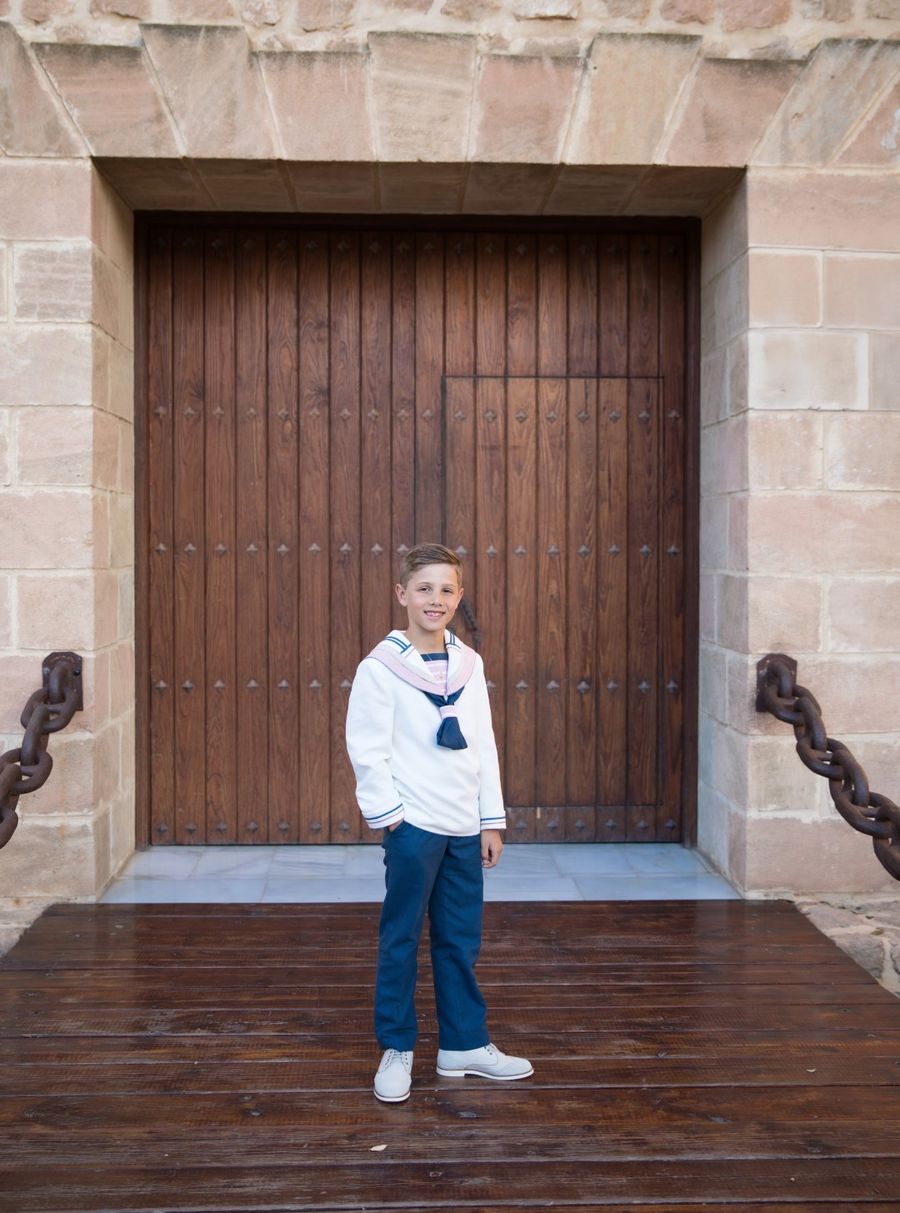 Niño de comunión ante un gran portón de madera