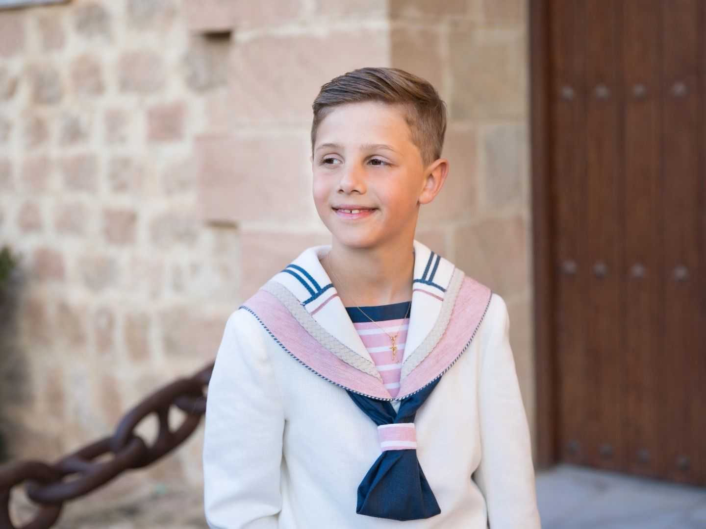Niño de comunión sonriendo junto a una puerta de piedra